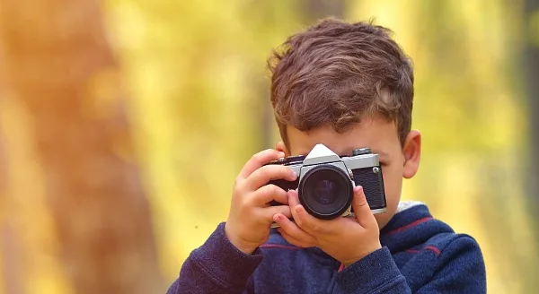 A young boy holding a vintage camera up to his face, taking a picture.
