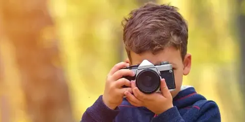 A young boy holding a vintage camera up to his face, taking a picture.