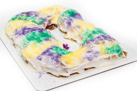 A King Cake dusted with purple, green, and yellow sugar on a white plate.