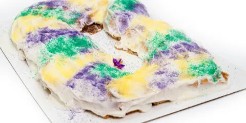 A King Cake dusted with purple, green, and yellow sugar on a white plate.