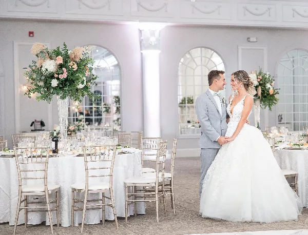 A bride with a styled updo and makeup standing with a groom in a wedding reception hall.