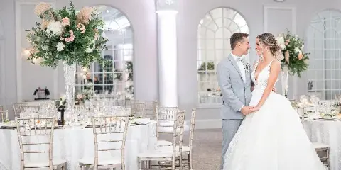 A bride with a styled updo and makeup standing with a groom in a wedding reception hall.