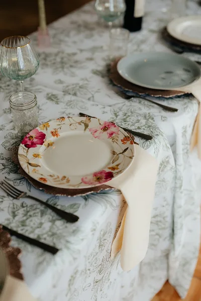A close-up of a wedding table setting featuring floral patterned plates, glassware, and a patterned tablecloth.
