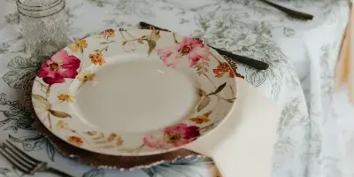 A close-up of a wedding table setting featuring floral patterned plates, glassware, and a patterned tablecloth.