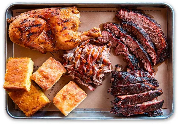 A metal tray filled with smoked brisket, pulled pork, ribs, and cornbread.
