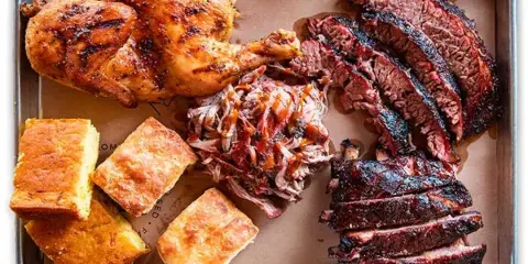 A metal tray filled with smoked brisket, pulled pork, ribs, and cornbread.
