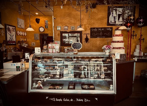 Interior view of a bakery with a glass display case of pastries and a tall, decorated wedding cake on the counter.