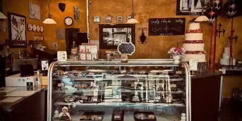 Interior view of a bakery with a glass display case of pastries and a tall, decorated wedding cake on the counter.