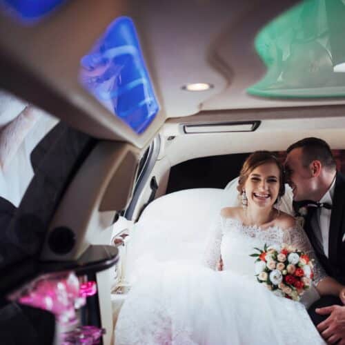 A bride and groom sitting together inside a luxury vehicle with ambient lighting.