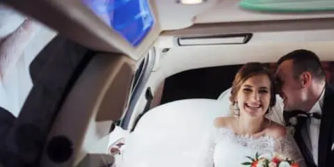 A bride and groom sitting together inside a luxury vehicle with ambient lighting.