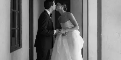 Black and white photograph of a bride and groom kissing in a corridor with hanging lanterns.