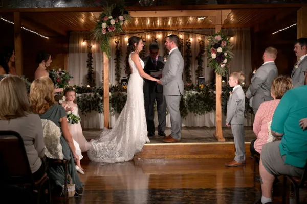 A bride and groom exchanging vows during a wedding ceremony under a decorated wooden arbor in an indoor event venue.