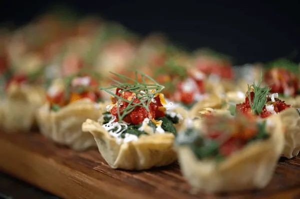 Close-up of prepared appetizer cups topped with red ingredients and herbs on a wooden board.
