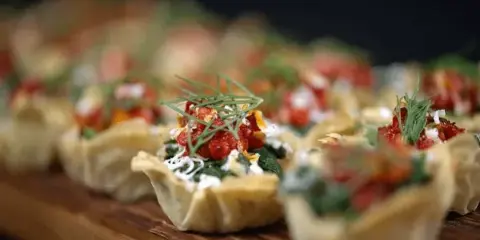 Close-up of prepared appetizer cups topped with red ingredients and herbs on a wooden board.