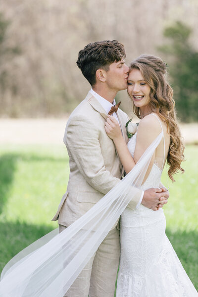A bride and groom in wedding attire sharing a kiss outdoors.