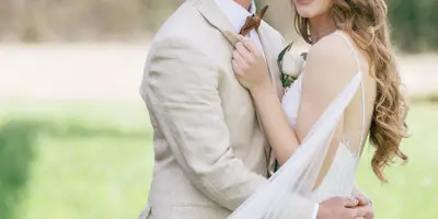 A bride and groom in wedding attire sharing a kiss outdoors.