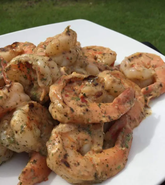 A white plate filled with cooked shrimp coated in a creamy herb sauce, set outdoors on a grassy surface.