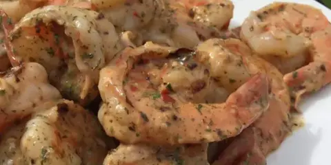 A white plate filled with cooked shrimp coated in a creamy herb sauce, set outdoors on a grassy surface.