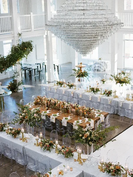 Wedding reception hall with long tables, floral arrangements, and a large crystal chandelier.