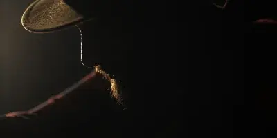 Dramatic low-key profile portrait of a bearded man wearing a hat, lit by a single rim light.