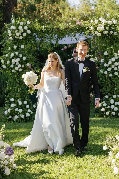 A bride and groom walking hand-in-hand after their wedding ceremony, with the bride holding a bouquet of white roses.