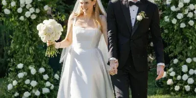 A bride and groom walking hand-in-hand after their wedding ceremony, with the bride holding a bouquet of white roses.