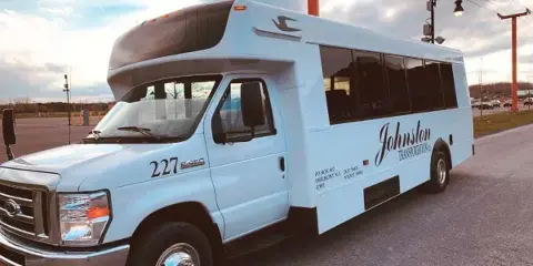 A white shuttle bus with Johnston Transportation branding parked in a lot.