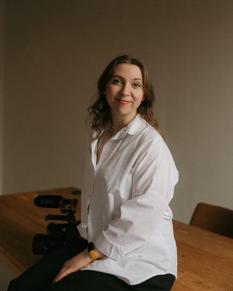 A woman in a white shirt sitting next to a professional video camera and microphone.