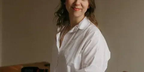 A woman in a white shirt sitting next to a professional video camera and microphone.