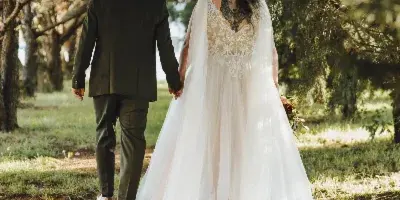A bride and groom walking hand-in-hand down a tree-lined path outdoors.