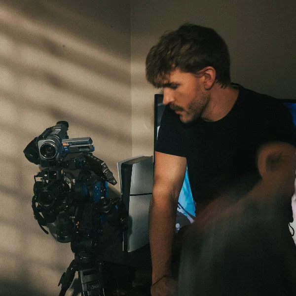A man in a black t-shirt working with professional video cameras and a computer monitor.