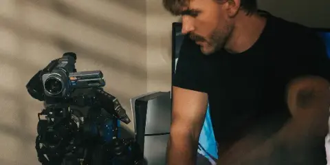 A man in a black t-shirt working with professional video cameras and a computer monitor.