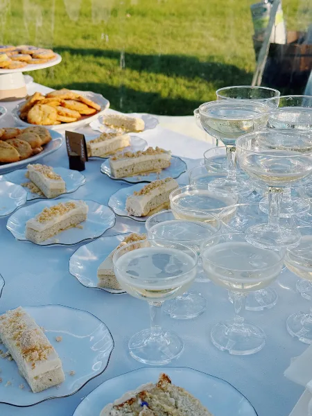 Outdoor catering table with plated layered desserts, cookies, and filled champagne coupes on a white tablecloth.