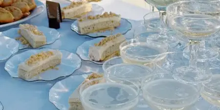 Outdoor catering table with plated layered desserts, cookies, and filled champagne coupes on a white tablecloth.