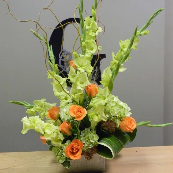 A tall floral arrangement with orange roses and lime-green gladiolus in a square vase