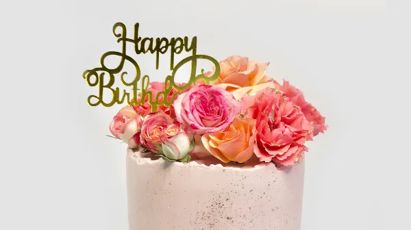 A custom cake decorated with pink and orange roses and a gold 'Happy Birthday' topper.