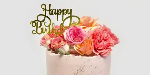 A custom cake decorated with pink and orange roses and a gold 'Happy Birthday' topper.