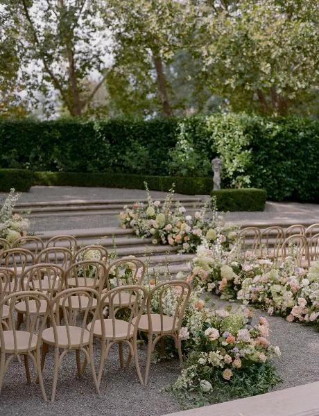 Outdoor wedding ceremony aisle decorated with rows of chairs and lush floral arrangements.