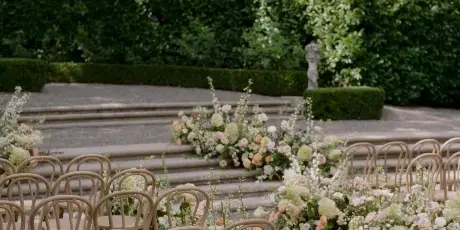 Outdoor wedding ceremony aisle decorated with rows of chairs and lush floral arrangements.
