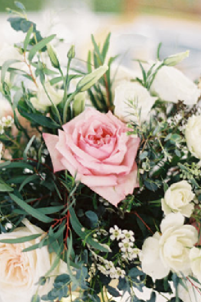 A floral arrangement featuring a pink rose, white roses, and greenery.