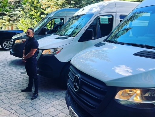 A driver standing in front of a row of white Mercedes Sprinter vans
