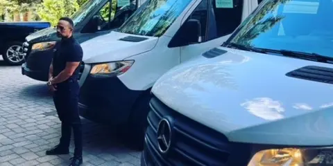 A driver standing in front of a row of white Mercedes Sprinter vans