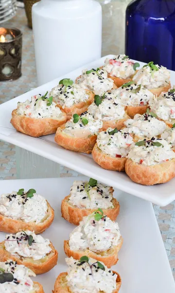 A platter of gourmet crab crostini appetizers garnished with microgreens and sesame seeds, served on a white rectangular dish.