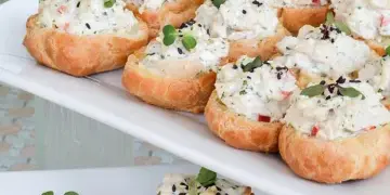 A platter of gourmet crab crostini appetizers garnished with microgreens and sesame seeds, served on a white rectangular dish.