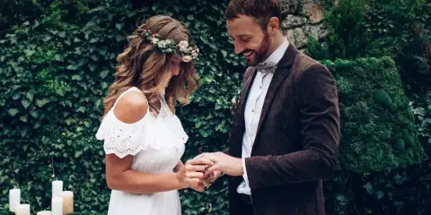 A bride and groom exchanging rings during an outdoor wedding ceremony.