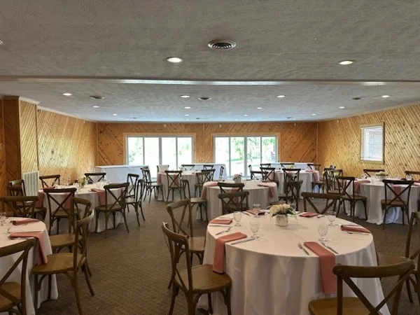 Interior of a rustic event venue with wooden walls and round tables set for a wedding reception.