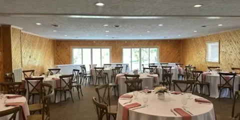 Interior of a rustic event venue with wooden walls and round tables set for a wedding reception.