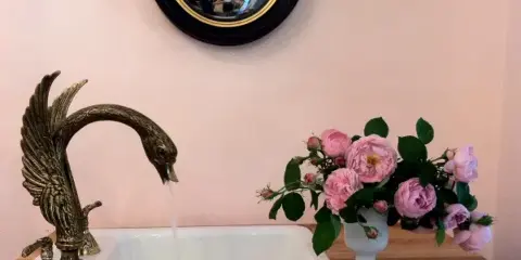A floral arrangement of pink roses in a white vase placed on a wooden counter next to a decorative bird-shaped faucet.