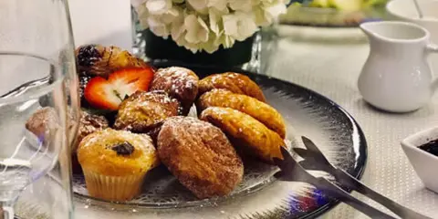 A plate of assorted pastries and muffins served on a table with a floral centerpiece.