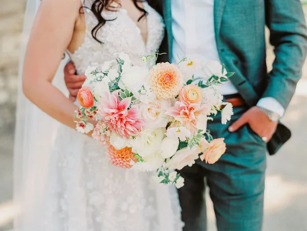 Bride holding a lush, custom wedding bouquet with pink and white flowers next to her groom.
